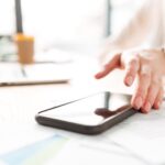 A phone on a desk with a woman's hand reaching for it