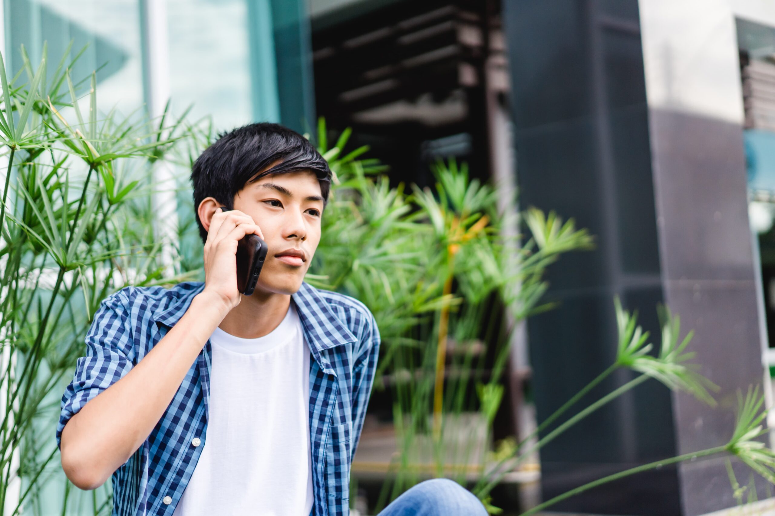 Teenage boy making a phone call sitting outside of a building