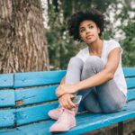 Teenage girl sitting on bench in a city with phone in her hand and looking beyond the camera