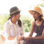 Two young women sitting outside next to each other and holding each other's hands