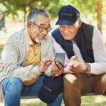 Two older veterans looking at a phone on a park bench