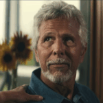 man with grey hair looking at someone next to him who has their hand on his shoulder