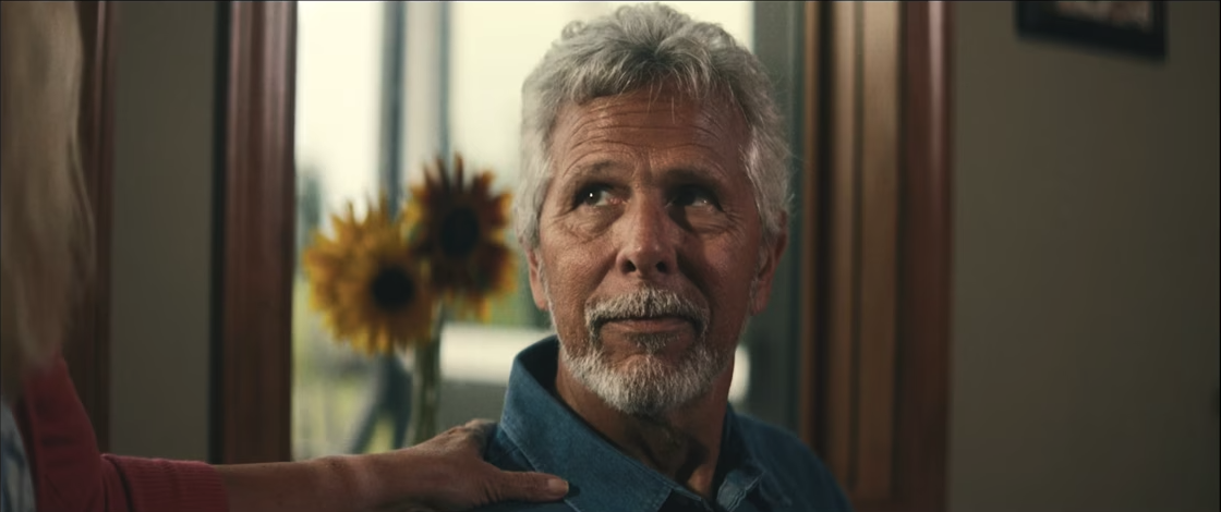 man with grey hair looking at someone next to him who has their hand on his shoulder