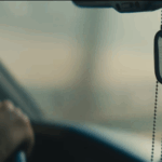 hands on a steering wheel with military dog tags hanging from rearview mirror