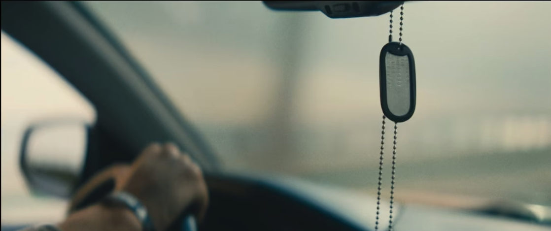 hands on a steering wheel with military dog tags hanging from rearview mirror
