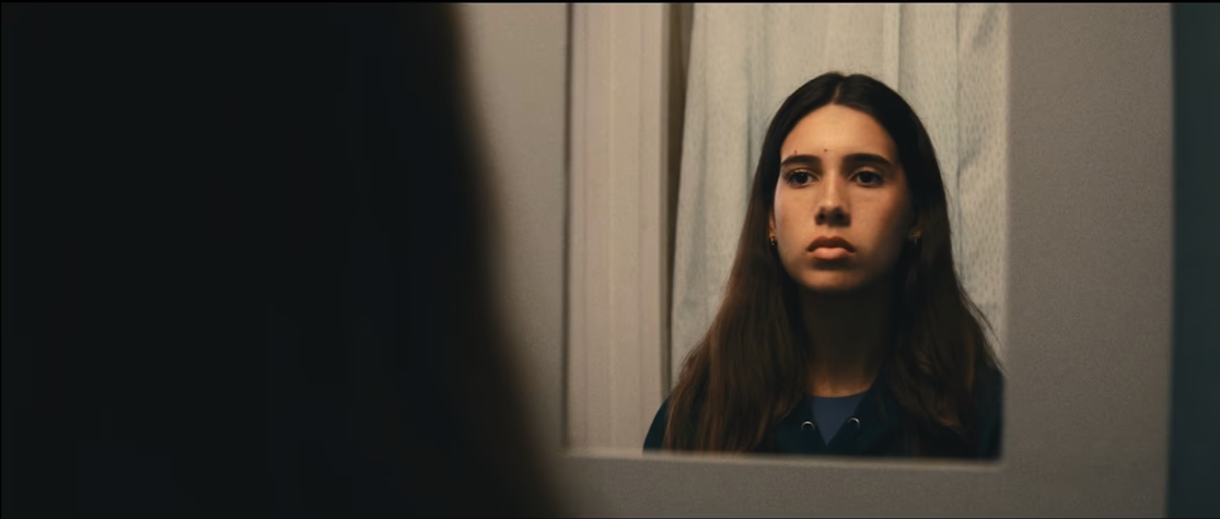 young girl with long brown hair staring blankly into a mirror