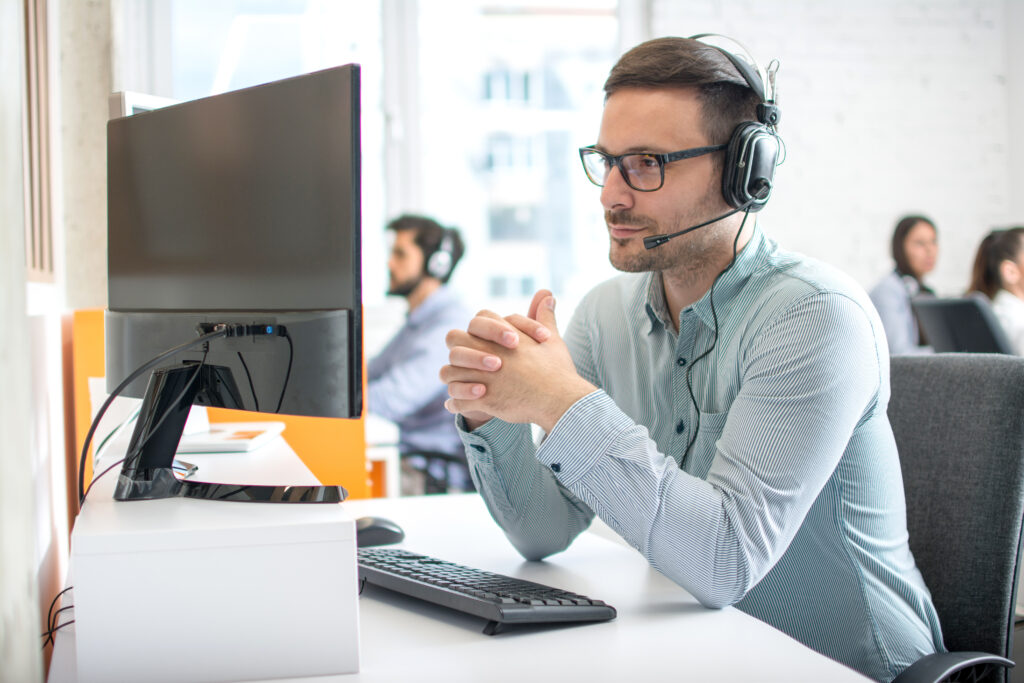 male talking on headset microphone while sitting at computer with hands clasped